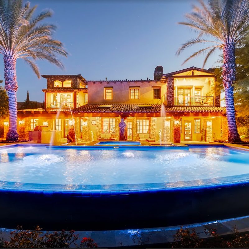 The exterior of an extravagant home with a large water fountain outside.